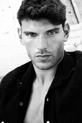 Obraz premium Portrait of handsome serious young man looking at camera with open black shirt revealing muscular pecs and sixpack abs