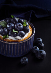 Blueberry dessert with cream, mint leaves and fresh berries at black background, close-up.