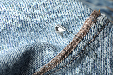 Metal safety pin on denim fabric, closeup