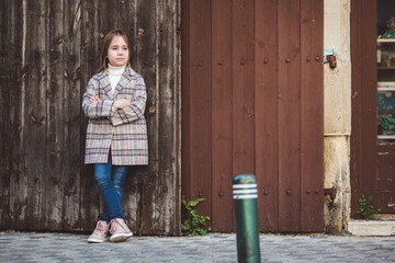 Portrait of adorable little fashionable girl outdoors near old fence