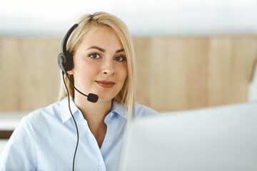 Blonde business woman sitting and communicated by headset in call center office. Concept of telesales business or home office occupation