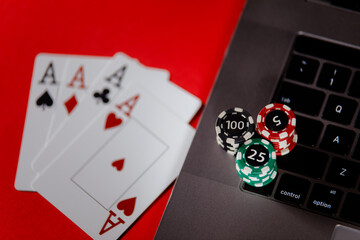 Poker cards, stacks of poker chips and laptop on a red background close-up. Poker online concept
