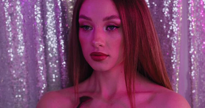 Glamour girl with perfect make-up in pink light. Closeup of beautiful young model on a brilliance background. The girl moves a brush by her collarbone .
