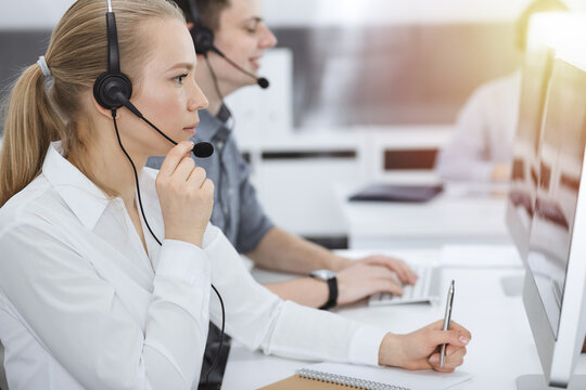 Call center. Group of casual dressed operators at work. Blond business woman in headset at customer service office. Telesales in business