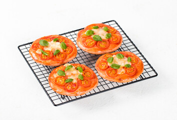 Mini-pizzas pink with beet juice added to the dough, small open pies with tomatoes, mozzarella and basil on a serving rack on a white background