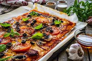 Pizza with white mushrooms, tomatoes, black olives, parmesan and mozzarella on wooden background

