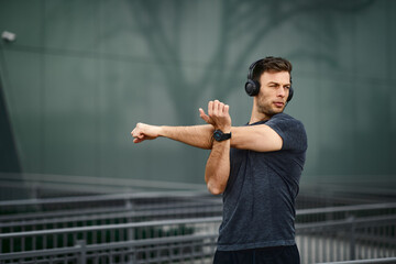 Young man stretching hands before the run in sports clothes and headphones on his head