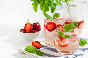 Homemade refreshing strawberry lemonade in glasses and jug with fresh strawberries and mint leaves. Summer drink 