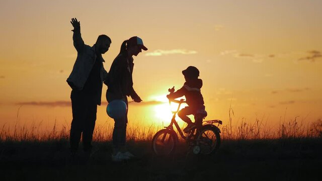 Happy family. Silhouette of a young family with a little son. Kid is learning to ride a bike. Silhouettes family with the child stand in a sunset. Teamwork, holding hands. Happy family concept.