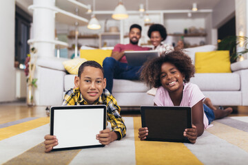 African american boy and girl lying on floor and using digital tablet. Family at home.