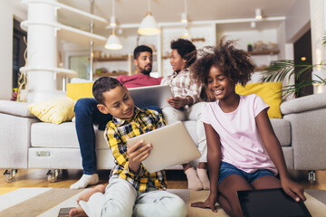 African american boy and girl lying on floor and using digital tablet. Family at home.