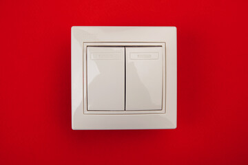 A square shaped white plastic light switch isolated on red