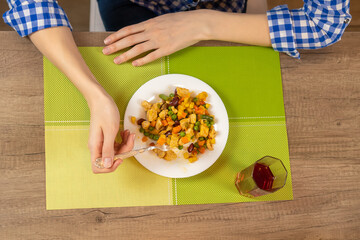 Women's hands eat with a fork fried pieces of meat and a variety of vegetables for lunch, next to a glass of juice. Concept of eating. Top view