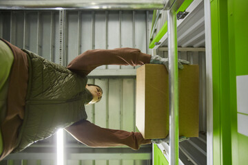 Low angle view of young woman putting cardboard box on the shelf in storage