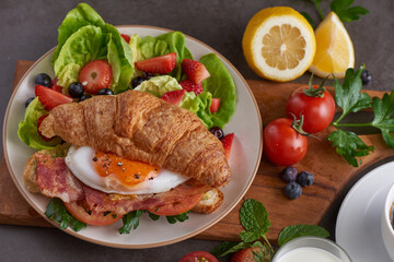 Delicious breakfast with fresh croissants, bacon sandwich with fried egg, tomato. milk served, coffee. strawberry, butterhead, blackberry salad. full american healthy breakfast top view.