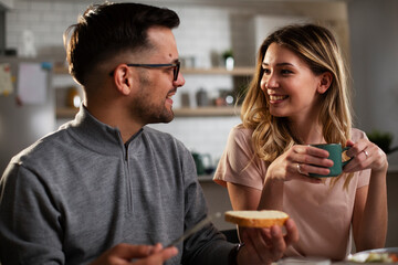 Beautiful young girl enjoying in breakfast with her boyfriend. Loving couple drinking coffee in the kitchen