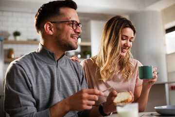 Beautiful young girl enjoying in breakfast with her boyfriend. Loving couple drinking coffee in the kitchen