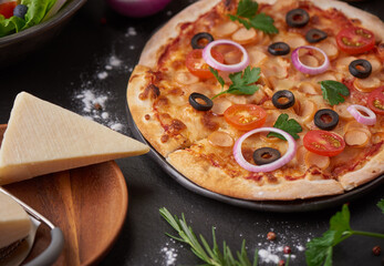 Italian pizza and pizza cooking ingredients on black concrete background. Tomatoes on vine, mozzarella, black olives, herbs and spices. Mixture pizza Italian food. Copy Space. Top view.