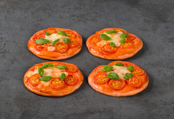 Children mini-pizzas pink with beet juice added to the dough, small open pies with cherry tomatoes, mozzarella and basil on a dark gray background