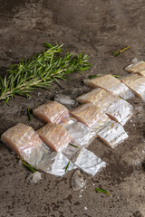 Raw frozen hake pieces with ice, sea salt, vintage knife and fresh rosemary