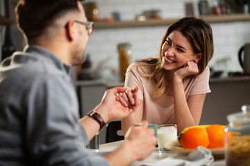 Beautiful young girl enjoying in breakfast with her boyfriend. Loving couple drinking coffee in the kitchen