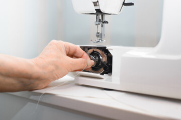 Preparing an electric sewing machine for work. A woman's hand installs a bobbin into the sewing equipment. Service, work at home, garment industry concept