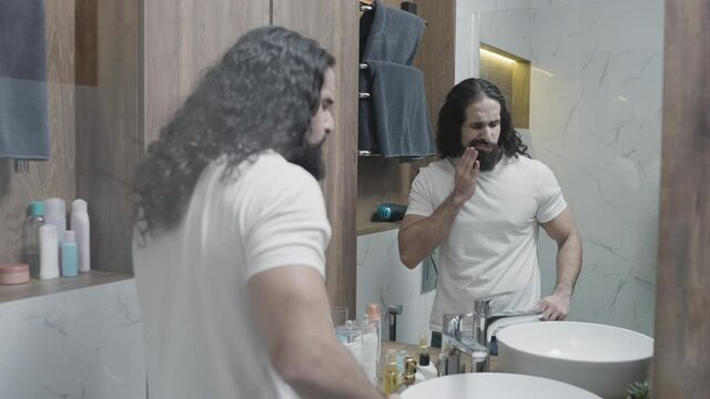 Turkish man feeling toothache, brushing teeth in bathroom, tooth decay, caries
