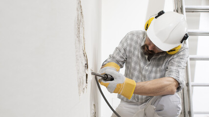 house renovation concept, construction worker breaks the old plaster of the wall with pneumatic air...