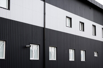 Black and white corrugated iron sheet used as a facade of a warehouse or factory with a windows....