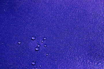 Wet blue background with water droplets scattering and purple light on the surface.