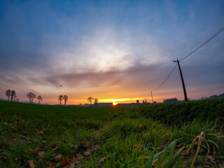 Fototapeta na wymiar Dramatic and colorful Sunrise or sunset on a field covered with young green grass and yellow flowering dandelions in springtime. Sunbeams making their way through the clouds. High quality photo