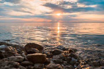 A picturesque landscape at a beautiful sunset or sunrise over a river with a cloudy sky background and rocks in the foreground.