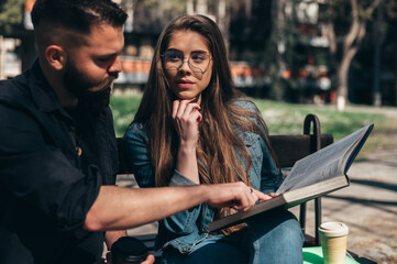 Two students sitting on a bench in a campus and studying for their exam