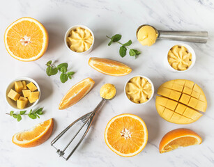 Orange and mango sorbet in bowl and in ice cream spoons and fruits spices on marble background. - obrazy, fototapety, plakaty
