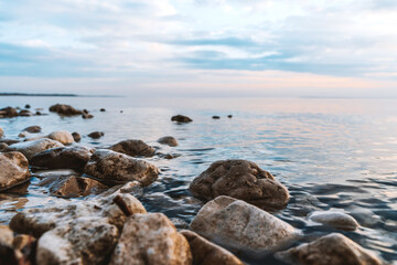 A picturesque landscape at a beautiful sunset or sunrise over a river with a cloudy sky background and rocks in the foreground.