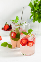 Homemade refreshing strawberry lemonade in glass and jug with fresh strawberries and mint leaves. Summer drink 