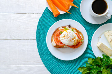 Sandwich with whole grain bread, goat cheese, fresh tomatoes and poached egg. Delicious simple breakfast. Proper nutrition. Top view, flat lay, copy space.
