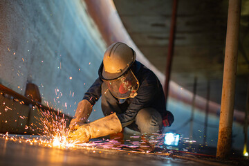 Male worker metal cutting spark on tank bottom steel plate with flash of cutting light close up wear protective gloves and mask