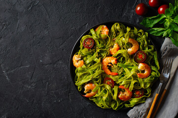 Green pasta with shrimp, basil and tomato on black background, top view, copy space, flat lay