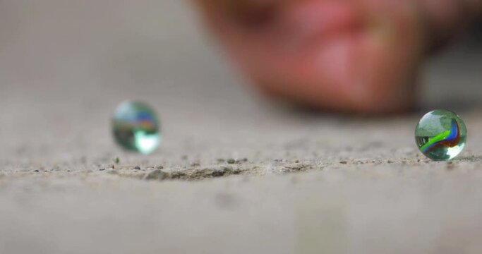 two glass marbles on the ground and a third comes and falls into the hole. Close up shot. 4K video.