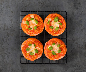 Children mini pizza pink with beet juice added to the dough, small open pies with cherry tomatoes, mozzarella and basil on a serving rack on a dark background top view