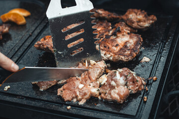 Man slices a pork neck, fragrant and richly seasoned with basil, pepper, salt and other herbs, which is fried on a granite slab over an open fire. Food preparation at a family event. Barbecue season