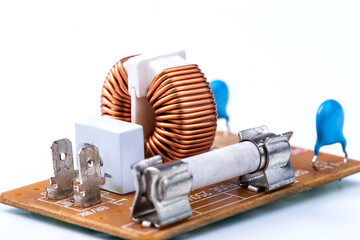 Close up of induction coil with copper wire winding soldered on printed circuit board and electric fuse isolated on white, toroidal inductor. Selective focus. - obrazy, fototapety, plakaty