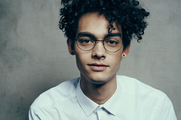 portrait of a nice guy with curly hair on a gray background and a light shirt glasses model close-up