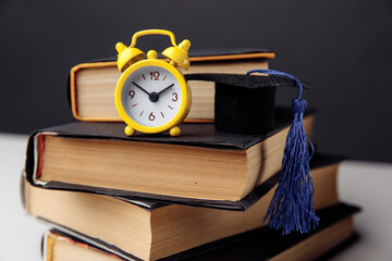 Yellow alarm clock, mini graduation cap and books on table. Education concept