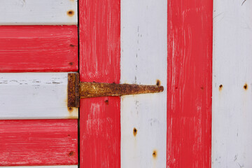 Section of red and white painted wooden hut with rusty hinge
