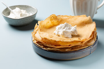 Stack of French crepes or thin pancakes with sour cream on blue background.