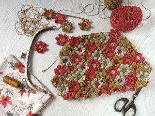 Crochet project of making crochet purse, joining crochet flowers one to another by hand sewing. Concept of art, design, and creativity. Needle, yarns, and scissors are in frame as tools. 