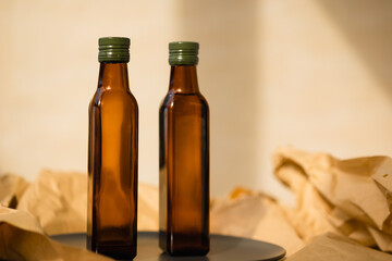 Fototapeta na wymiar Two glass brown transparent faceted bottles without labels empty and full with vegetable oil with green metal caps stands on a black plate on paper. Salad dressing. Linseed, olive oil in sun light