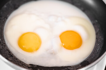Cooked small fried eggs with two bright round raw yolks in a black skillet. Simple breakfast. Top view, close-up, minimalistic
